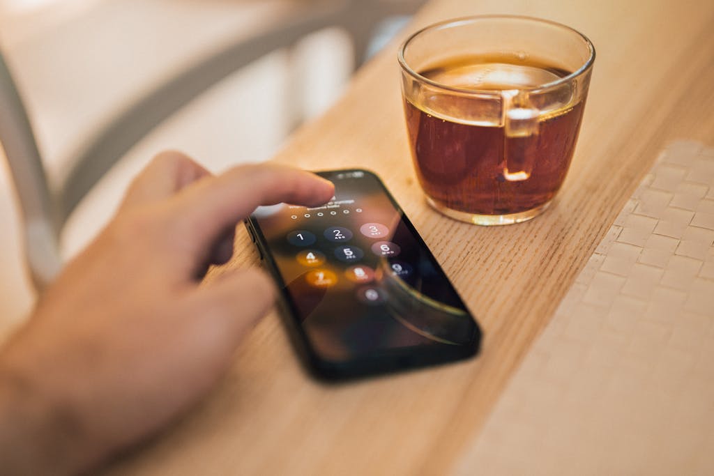 Close-up of hand unlocking a smartphone next to a cup of tea on a wooden table, emphasizing technology and security.